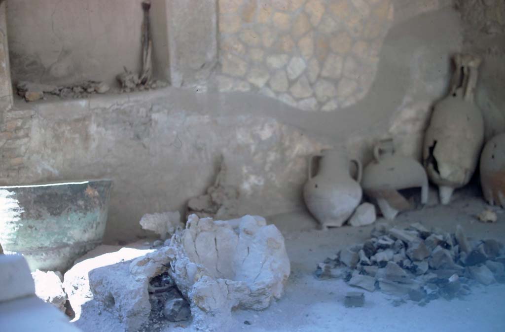 VI.12 Herculaneum, 7th August 1976.
Looking towards south wall of shop-room, with crucible, in centre, and collection of pots/amphorae, etc.
Photo courtesy of Rick Bauer, from Dr George Fay’s slides collection.